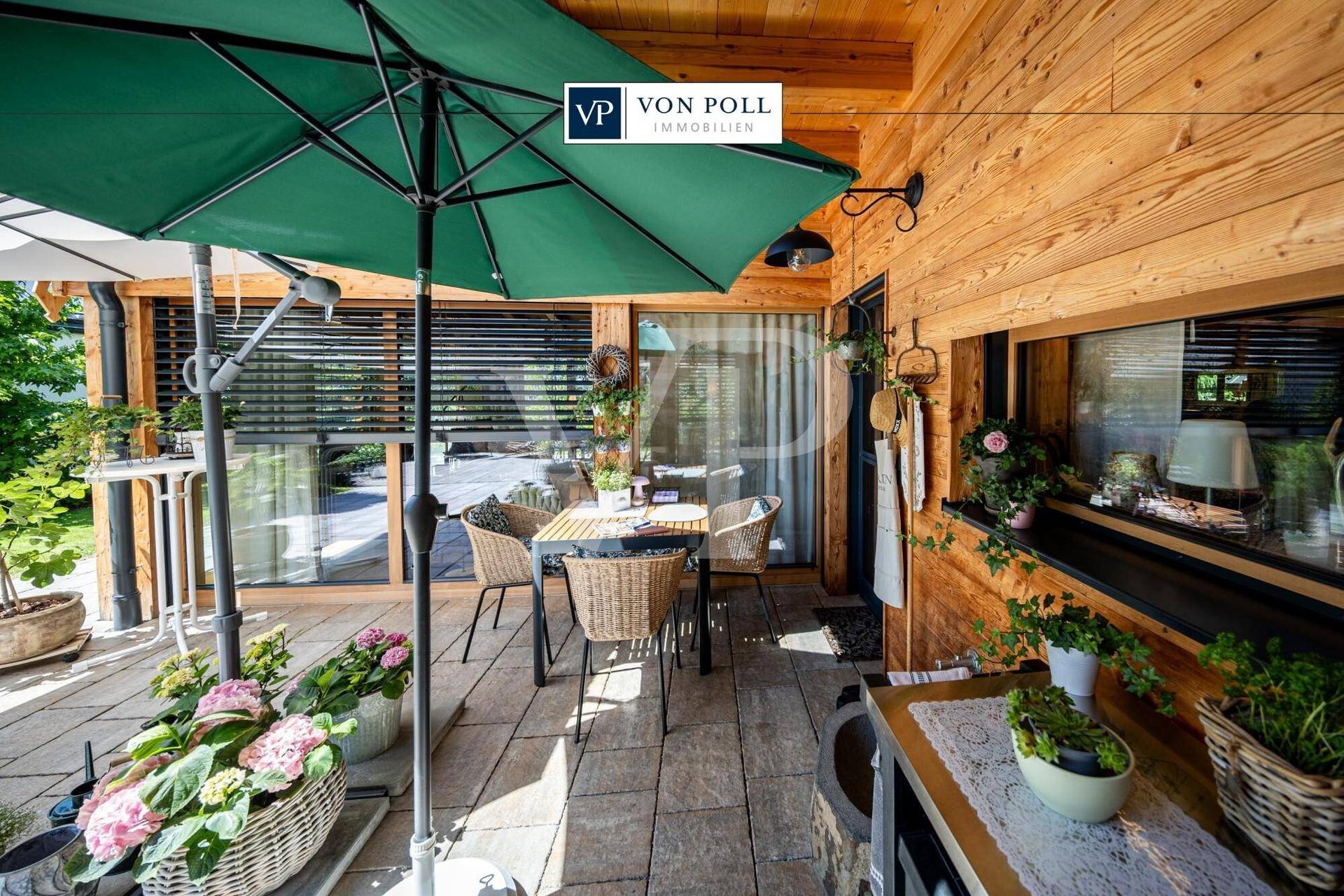 Sonniger Terrassenbereich mit Gartenmöbeln, großem Sonnenschirm und Zugang zum Innenbereich.