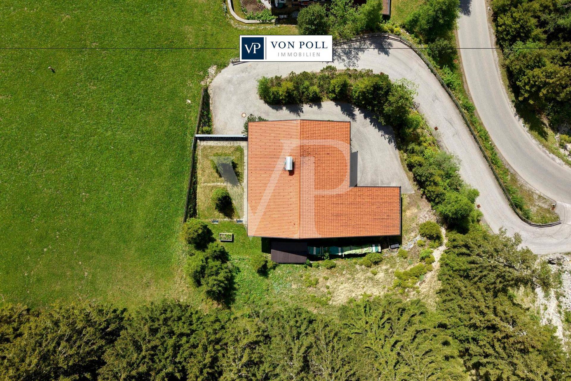 Luftaufnahme des Chalets mit rotem Dach, umgeben von grünen Wiesen und bewaldeten Berghängen.
