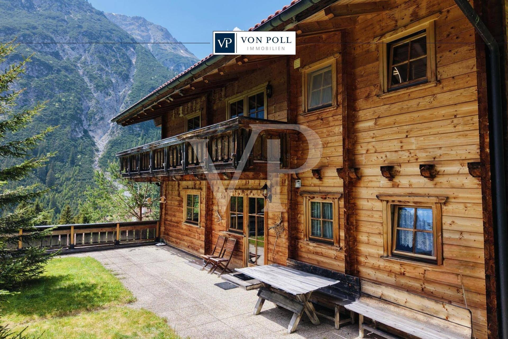 Geräumige Terrasse mit Holztisch und Balkon, umgeben von alpiner Natur und Bergblick.