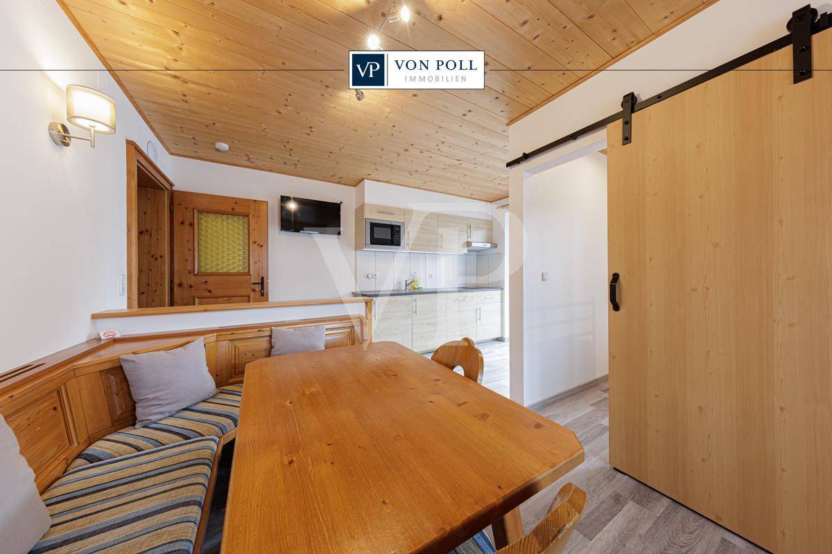 Rustikaler Wohn-Essbereich mit Holztisch, Eckbank und einer kleinen Küchenzeile.