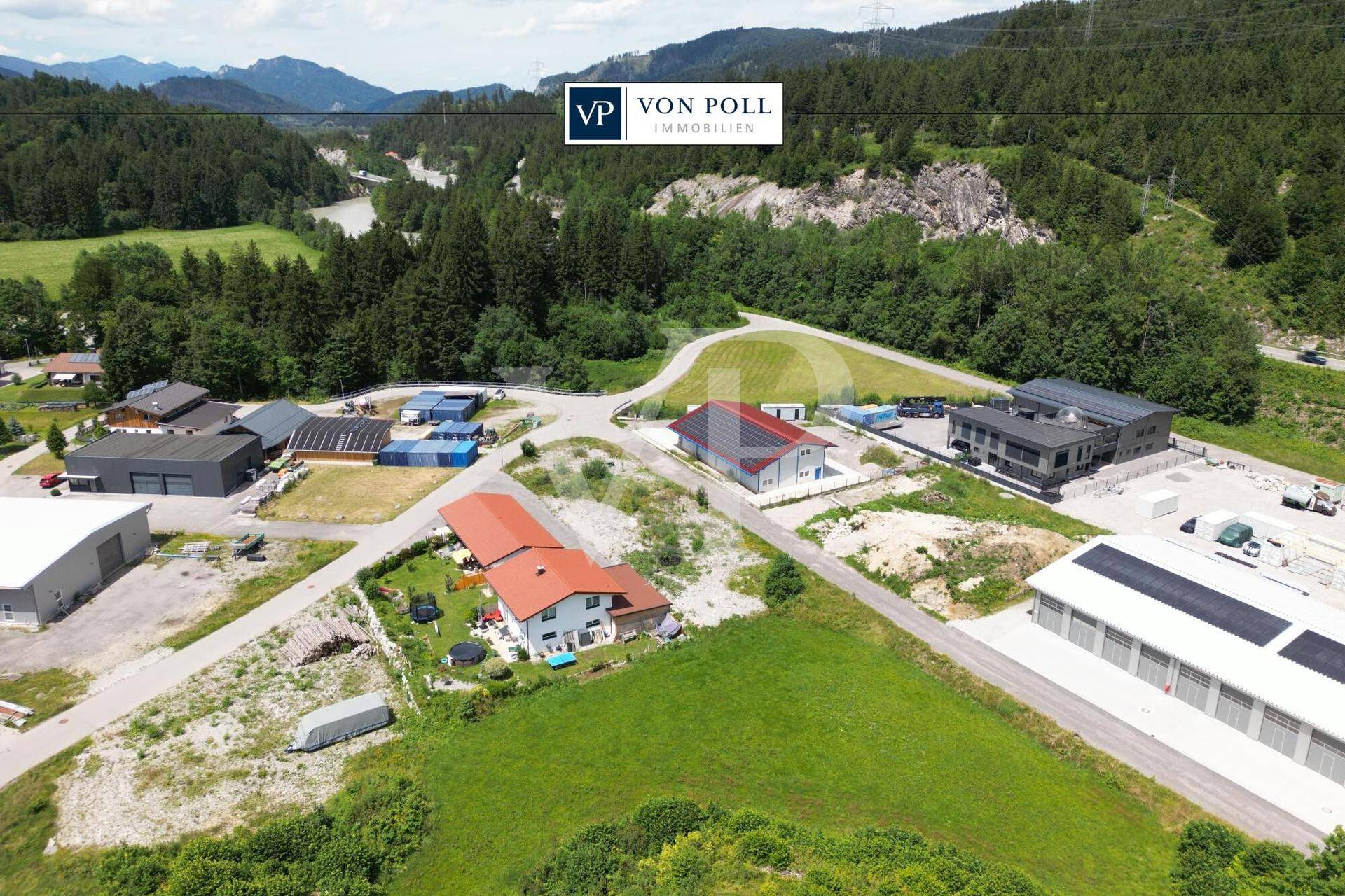 Luftaufnahme einer malerischen Landschaft mit Fluss, dichten Wäldern, Bergen und einigen Gebäuden im Vordergrund.