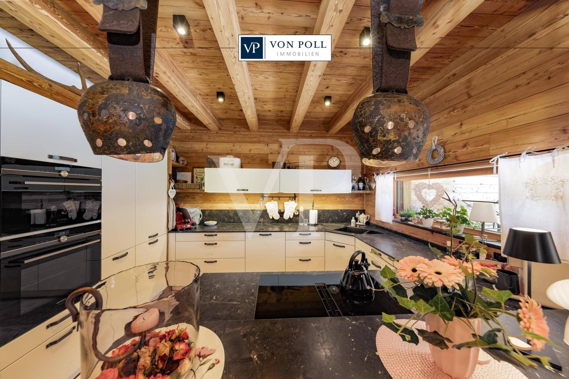 Moderne Küche im alpinen Stil mit weißen Schränken, dunkler Arbeitsplatte und traditionellen Glocken als Dekoration.