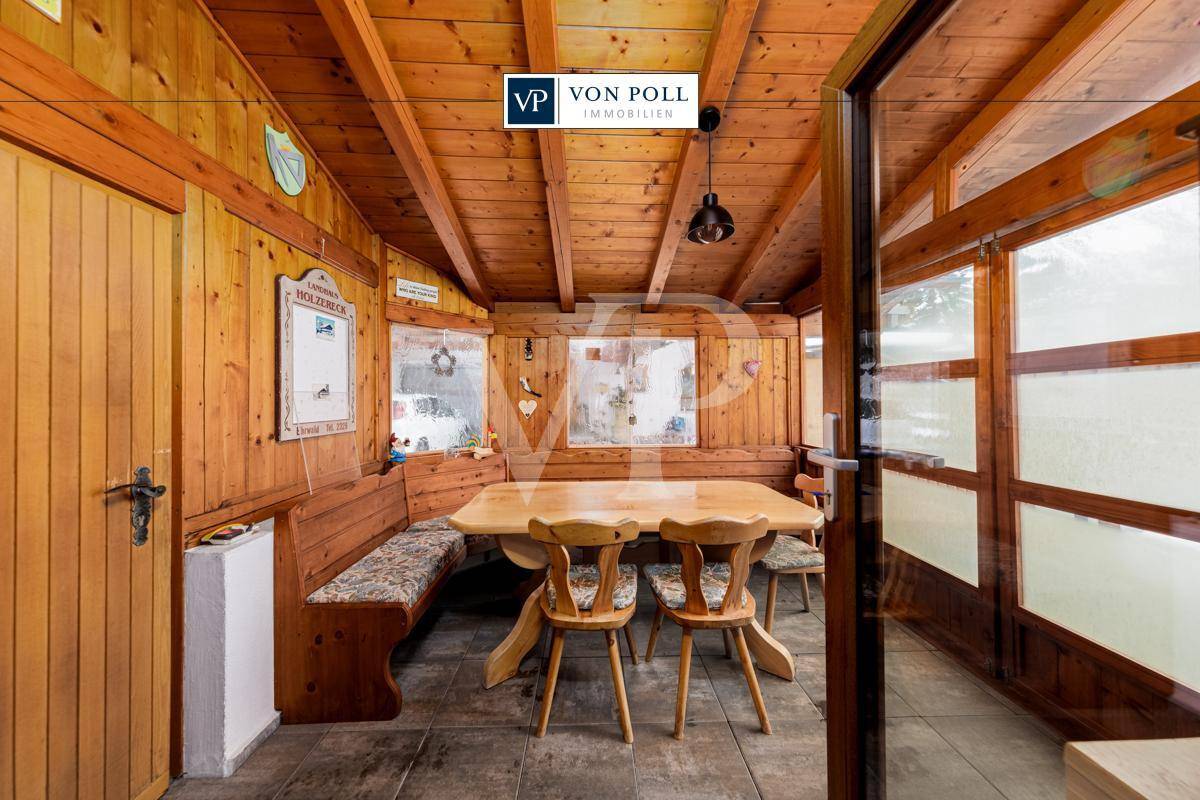 Rustikaler Wintergarten mit viel Holz, einer gemütlichen Sitzecke und Blick nach draußen.