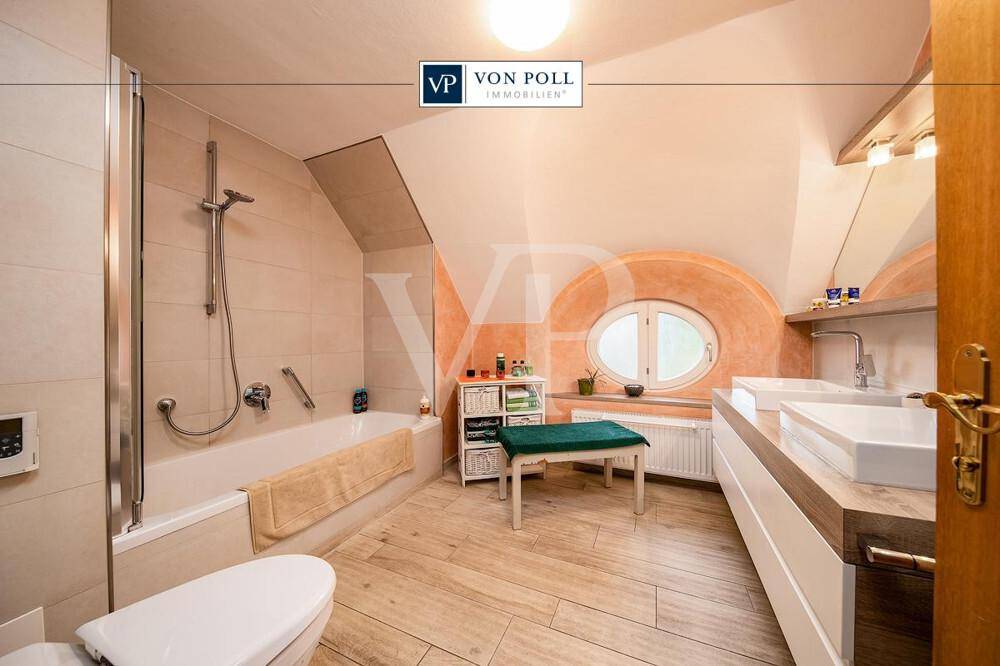 Modernes Badezimmer mit Badewanne, Dusche, Doppelwaschbecken und ovalem Fenster unter Dachschräge.