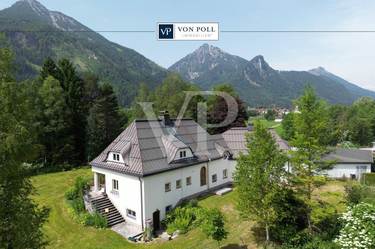 Freistehendes Haus mit weißer Fassade, umgeben von Grünflächen und beeindruckendem Bergblick.