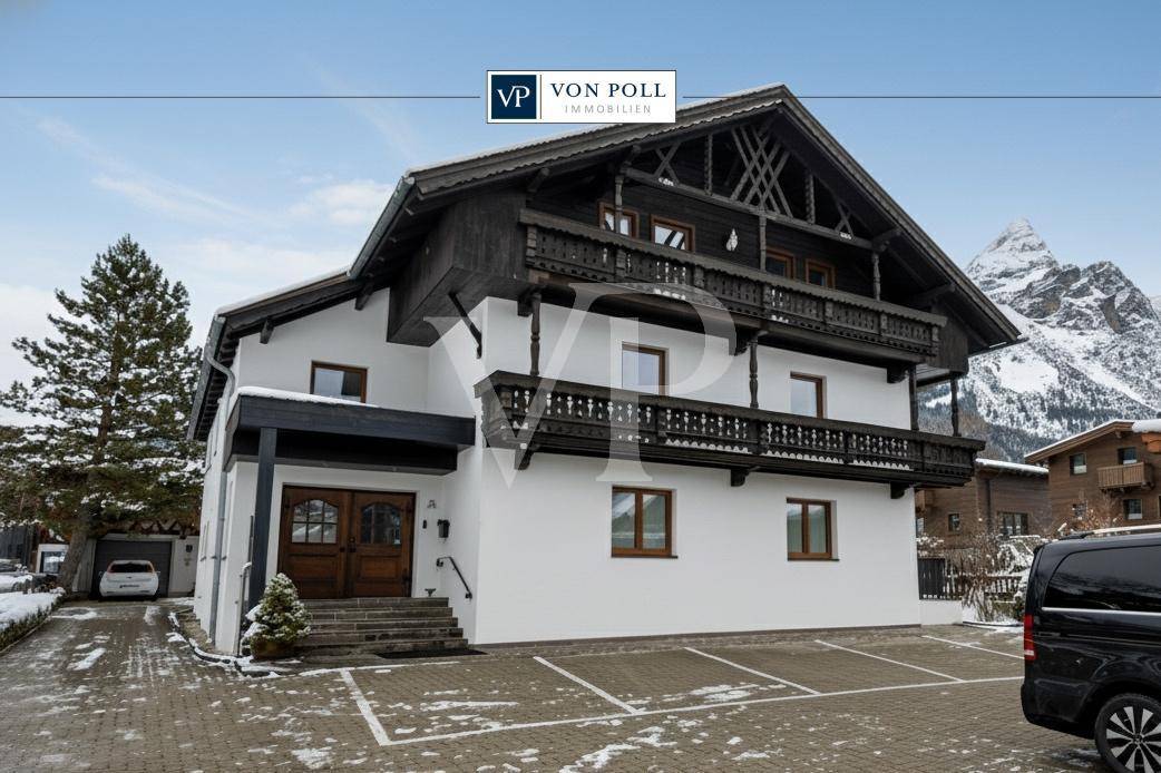 Traditionelles Chalet-Haus mit Holzbalkonen und schneebedeckten Bergen im Hintergrund an einem sonnigen Tag.