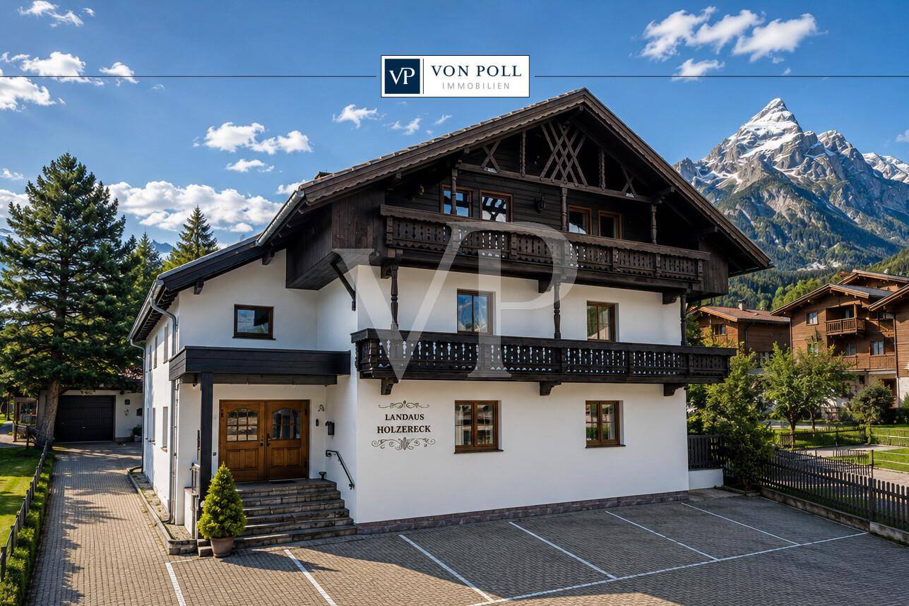 Charmantes Landhaus im alpinen Stil mit Holzbalkonen und beeindruckendem Bergblick an einem sonnigen Tag.