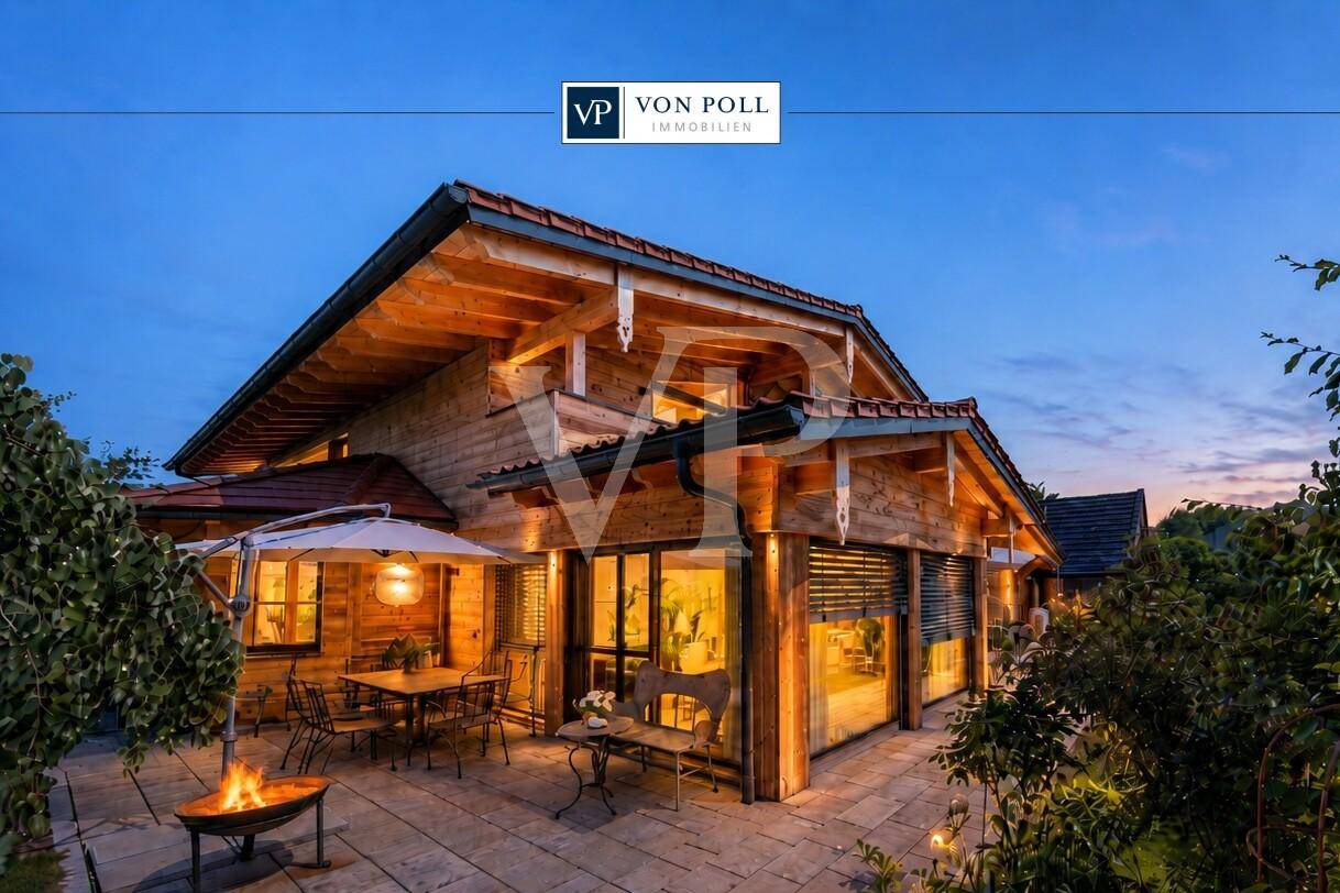 Charmantes Holzhaus im alpinen Stil mit beleuchteter Terrasse und Feuerstelle bei Sonnenuntergang.