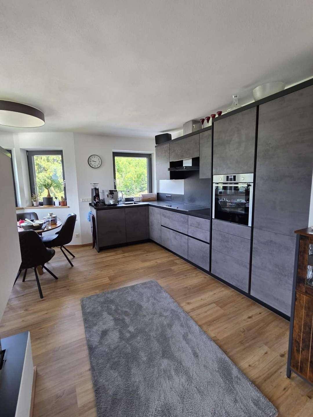 Moderne Küche mit grauen Schränken, Holzboden und integriertem Essbereich mit Blick ins Grüne.