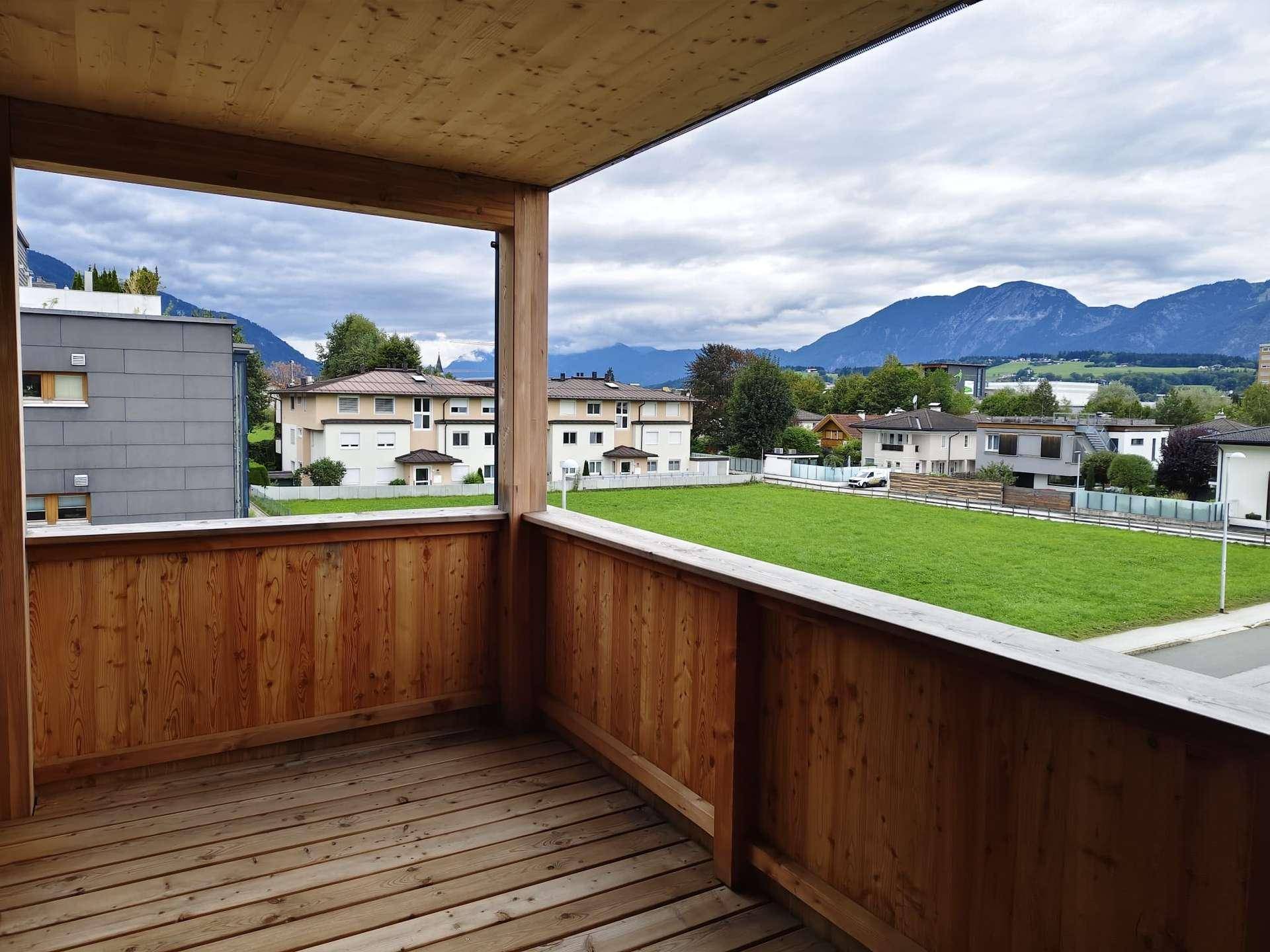 Geräumiger Holzbalkon mit Bergblick und Blick auf eine grüne Wiese.