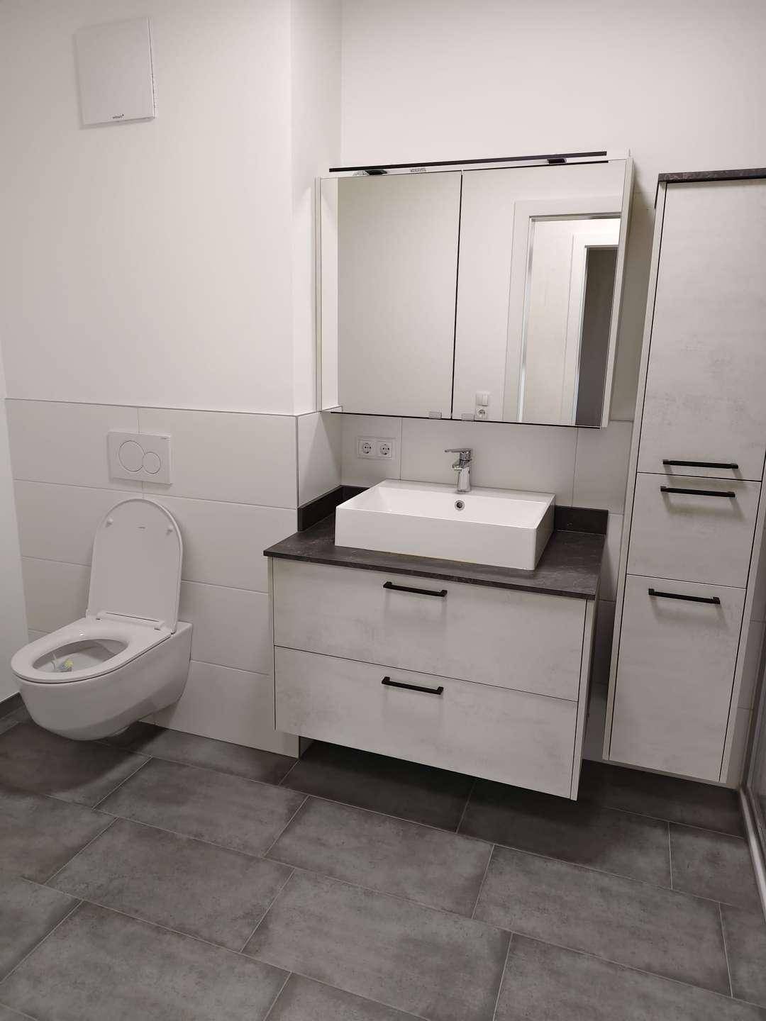 Zeitgemäßes Badezimmer mit wandhängendem WC, Einzelwaschbecken und Spiegelschrank.