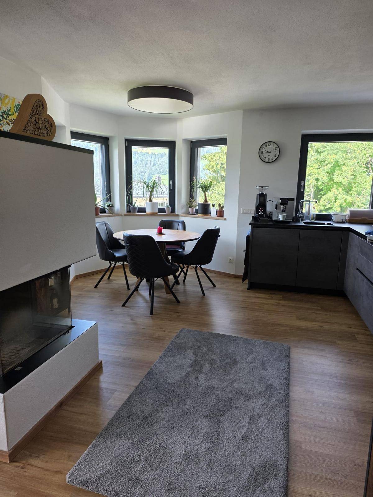 Heller Essbereich mit rundem Tisch, vielen Fenstern und einem modernen Kamin im Hintergrund.