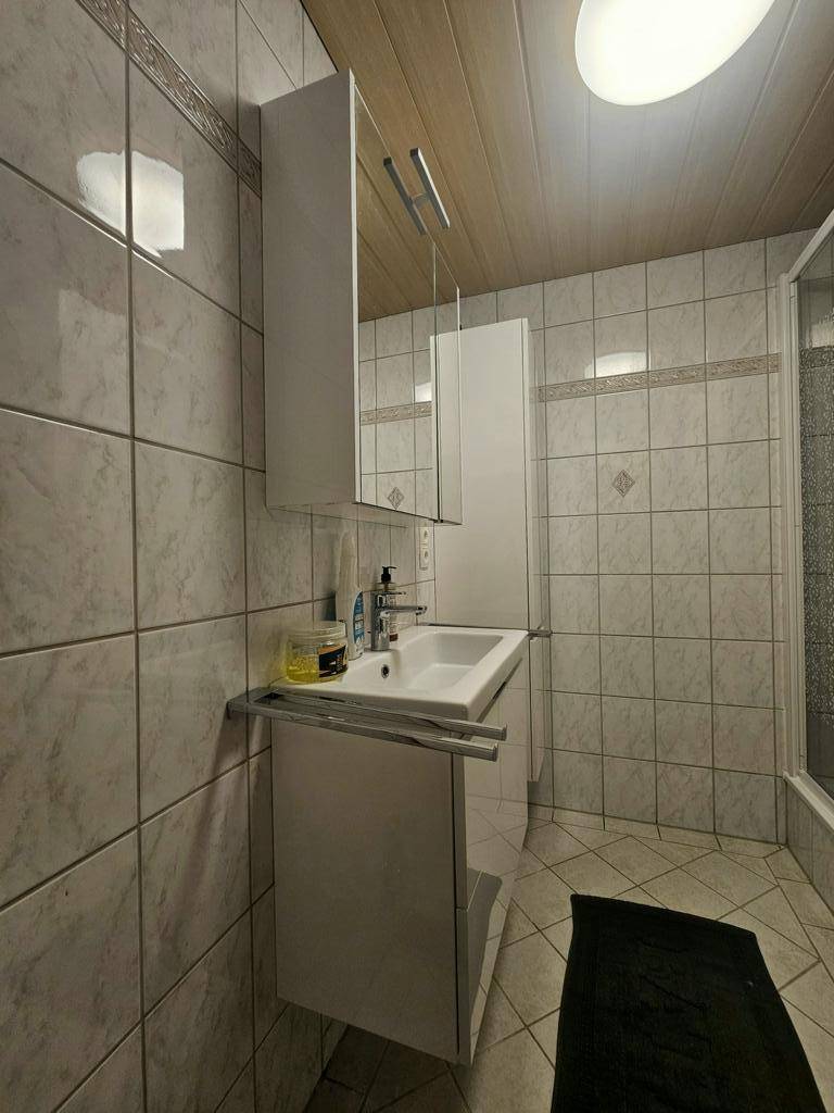 Gefliestes Badezimmer mit Duschbereich, Waschbecken und Spiegelschrank, bietet praktischen Stauraum.