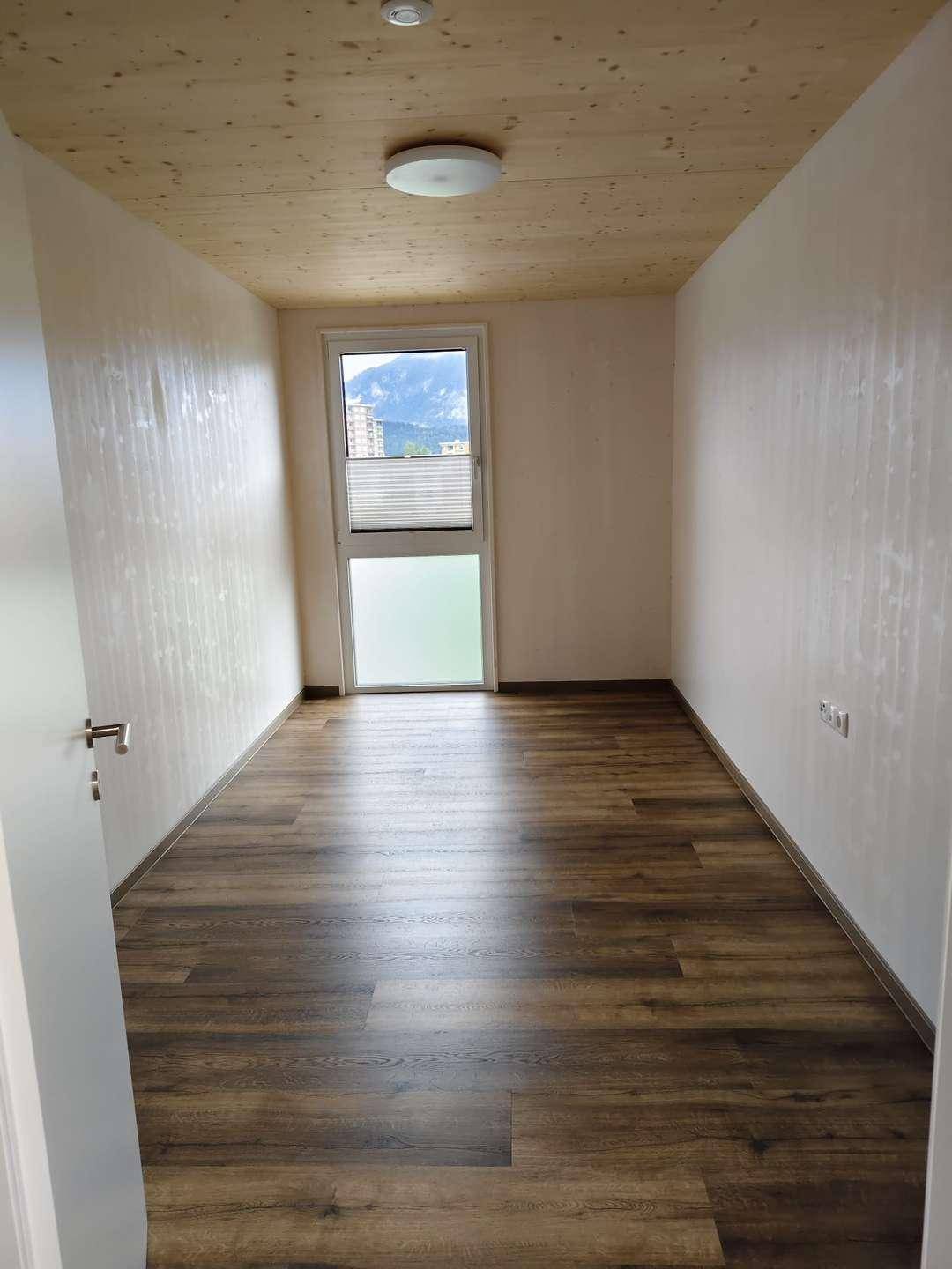 Helles Schlafzimmer mit Laminatboden, Holzbalkendecke und Fenster mit Blick auf die Berge.
