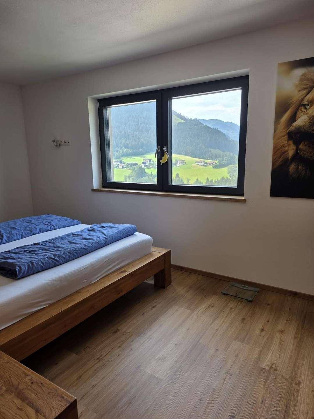 Gemütliches Schlafzimmer mit Holzbett, Parkettboden und weitem Blick auf die grüne Landschaft.
