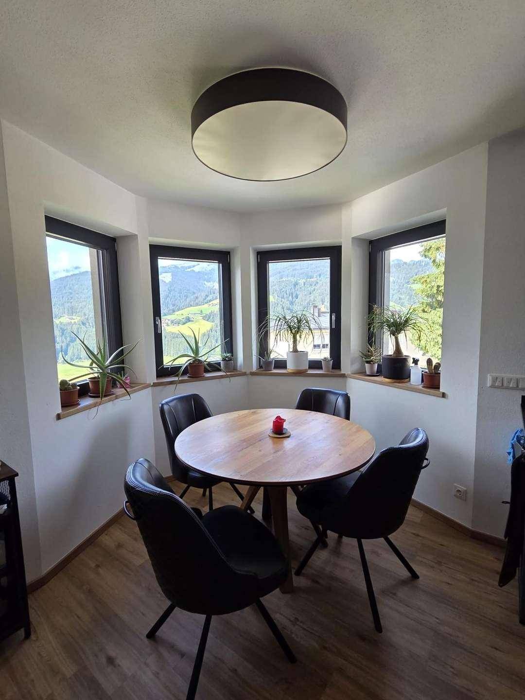 Heller Essbereich mit Holztisch, modernen Stühlen und Panoramablick auf die umliegenden Berge.