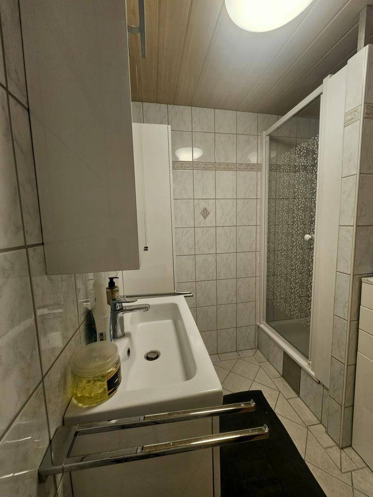 Badezimmer mit Duschkabine, Waschbecken und hellen Fliesen, ausgestattet mit einem Spiegelschrank.