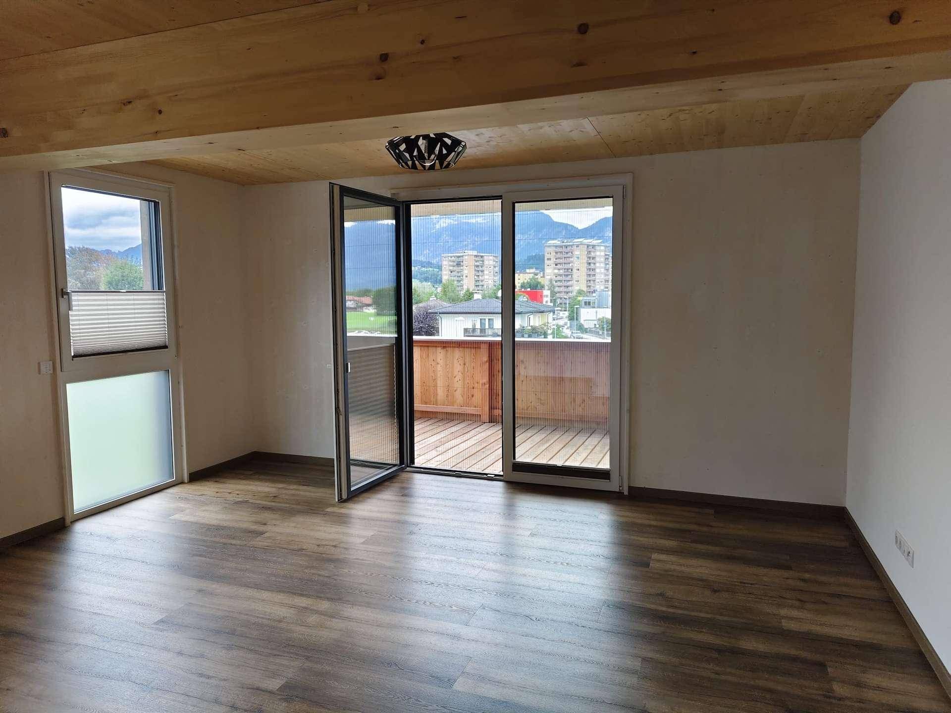 Heller Wohnraum mit Holzbalkendecke, Laminatboden und großem Fenster mit Blick auf die Umgebung.