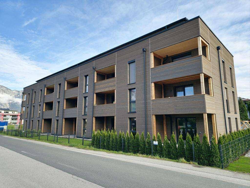 Ansicht eines neuen Wohngebäudes mit Holzverkleidung, Balkonen und gepflegter Hecke.