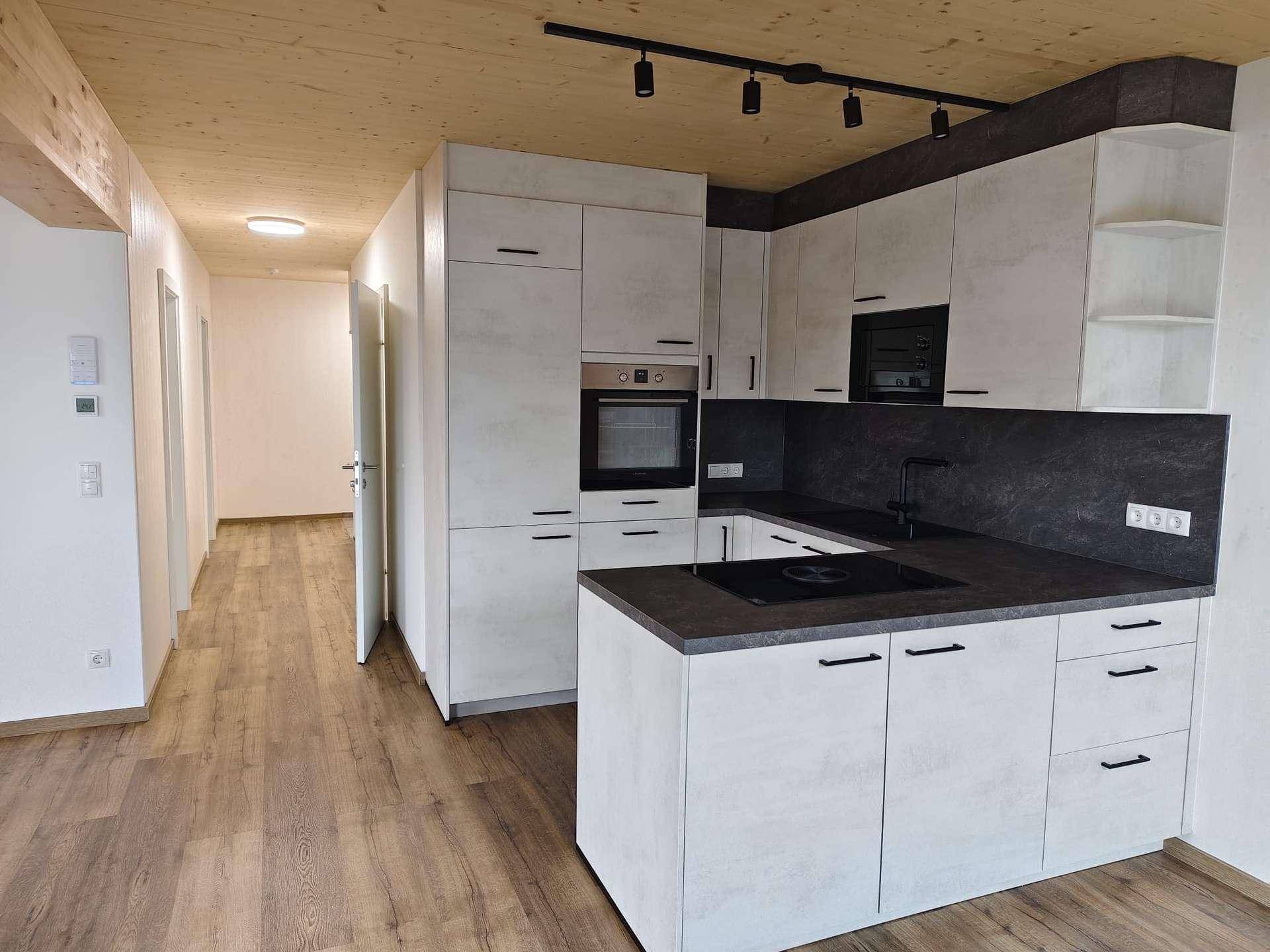 Moderne Einbauküche mit Kochinsel, dunkler Arbeitsplatte und Holzbalkendecke in einem offenen Wohnbereich.