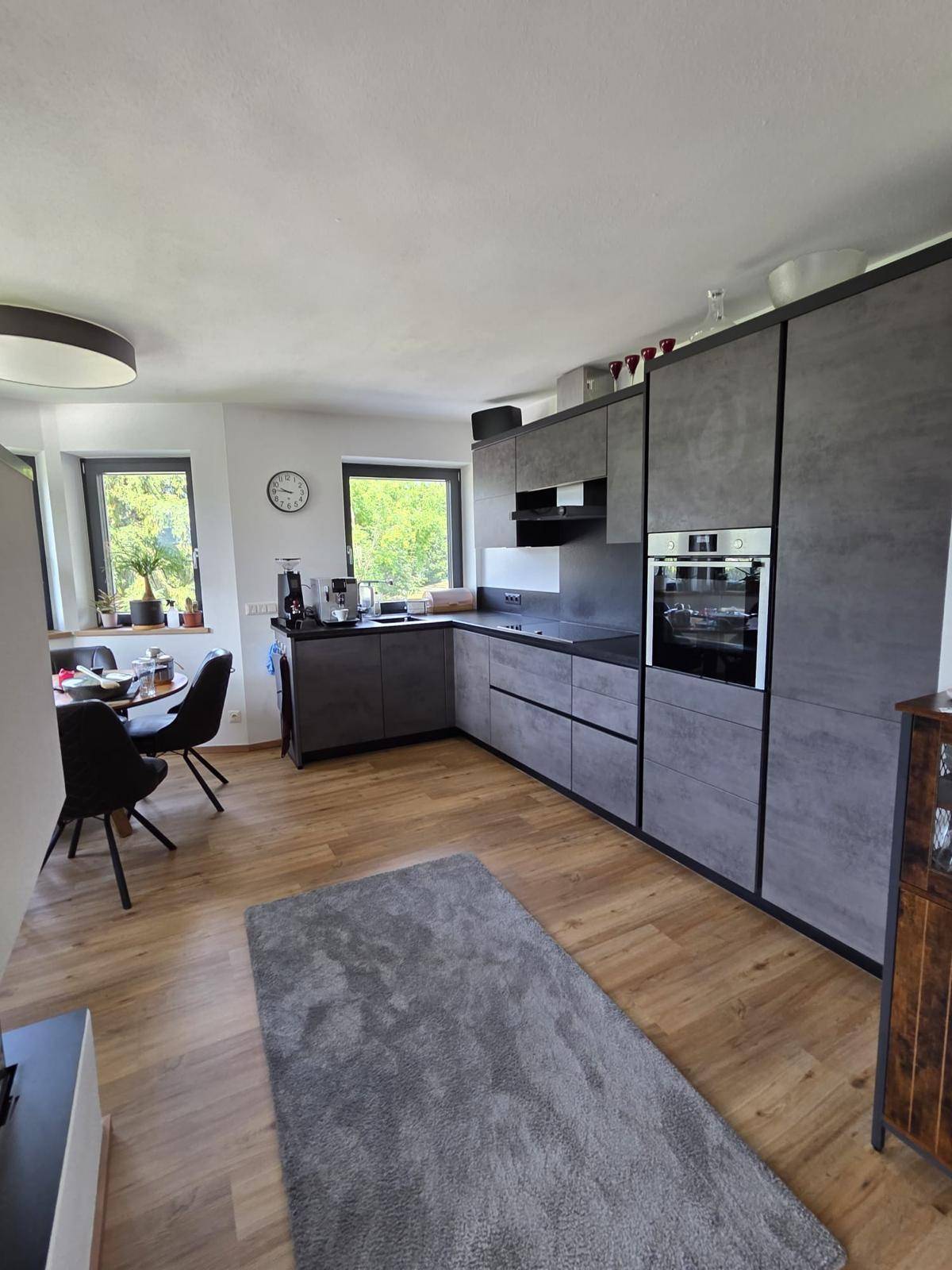 Moderne Küche mit grauen Schränken, Holzboden und integriertem Essbereich mit Blick ins Grüne.