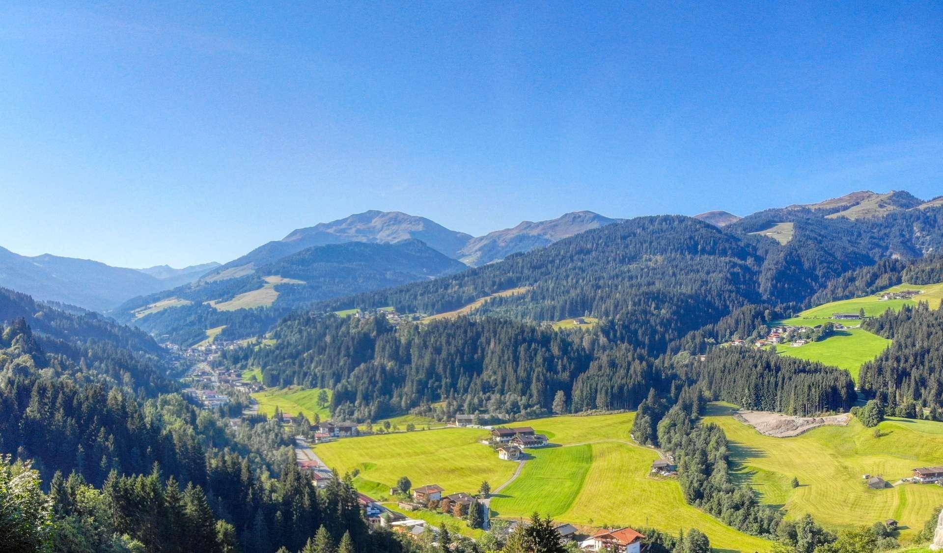 Weitläufige Alpenlandschaft mit grünen Tälern, dichten Wäldern und malerischen Dörfern.