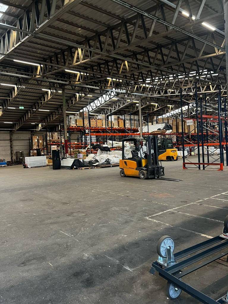 Große Lagerhalle mit Gabelstaplern, Palettenregalen und Waren, bereit für Logistikabläufe.