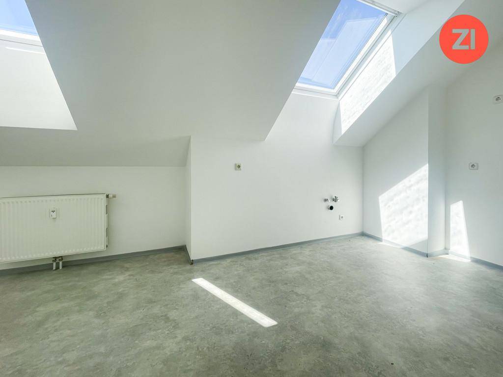 Heller Raum mit Betonboden, Dachschrägen und sichtbaren Anschlüssen für Installationen.
