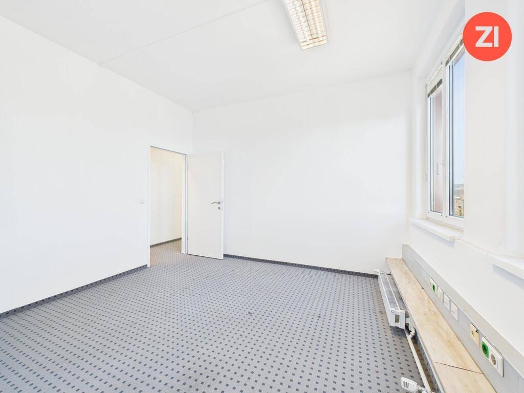 Leeres Büro mit Teppichboden, weißen Wänden und einem Fenster, das Tageslicht hereinlässt.