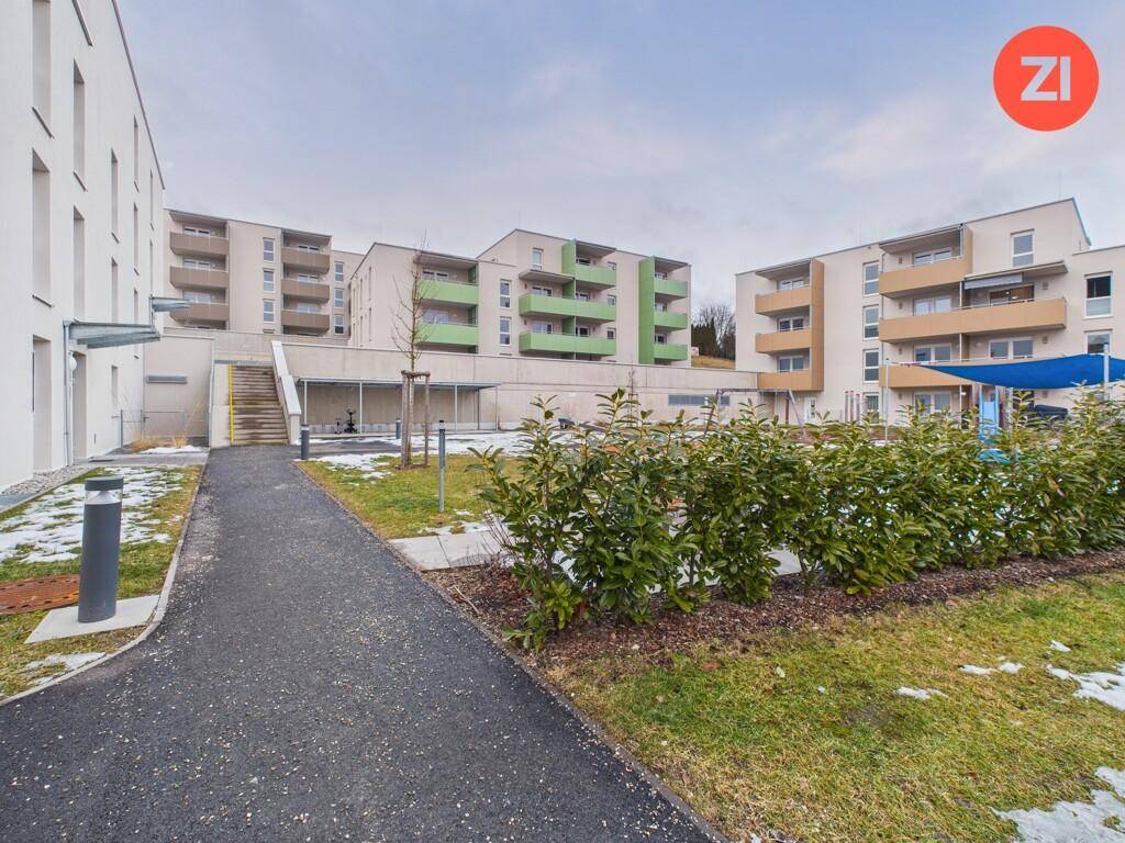 Moderne Wohngebäude mit grünen Balkonen und einer gepflegten Außenanlage mit Rasen und Büschen.