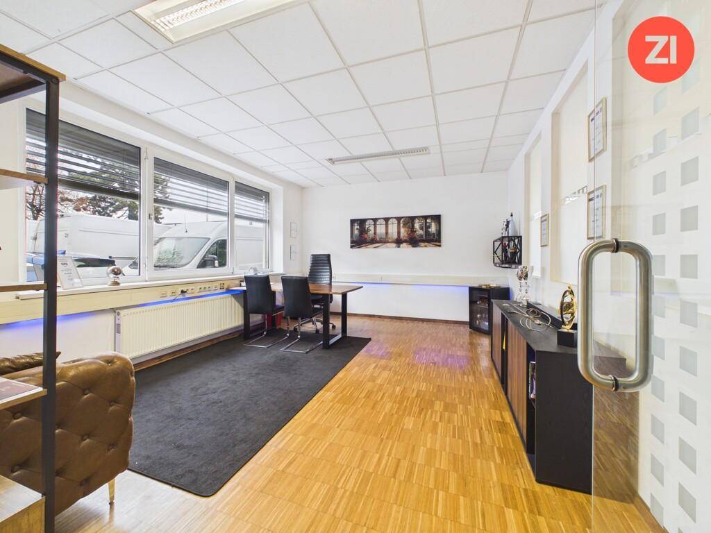 Großes Büro mit Holzboden, dunklem Teppich, Sideboards und indirekter Beleuchtung.