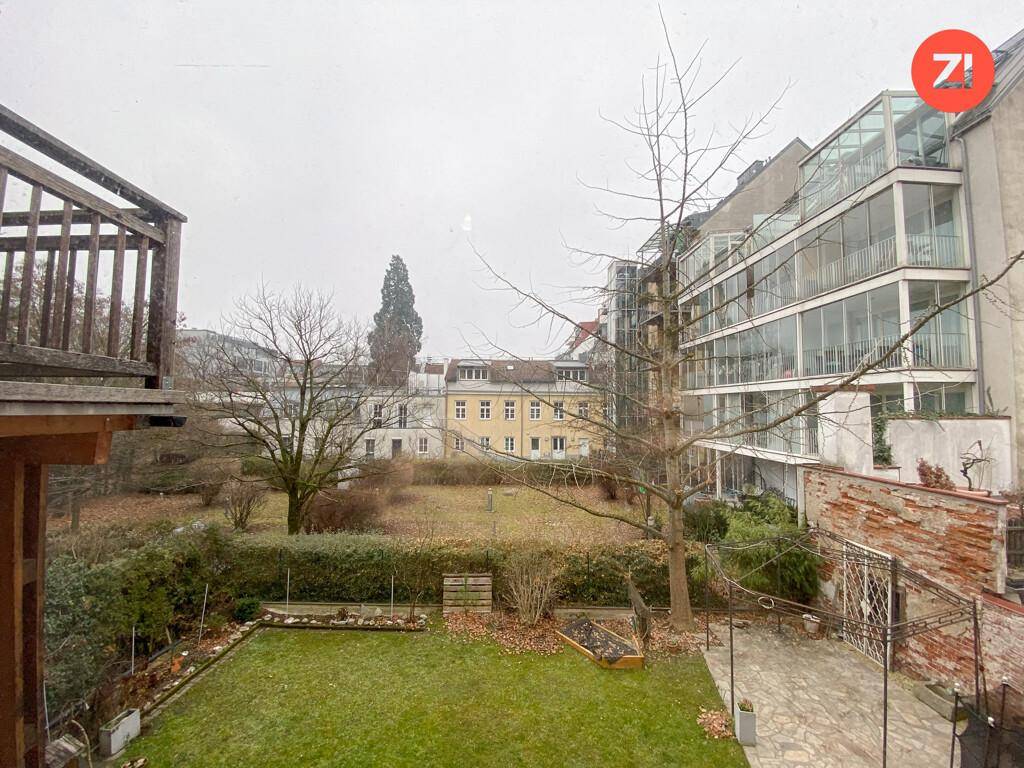 Gartenbereich mit Rasen und Bäumen, umgeben von modernen Gebäuden mit Glasfassaden.