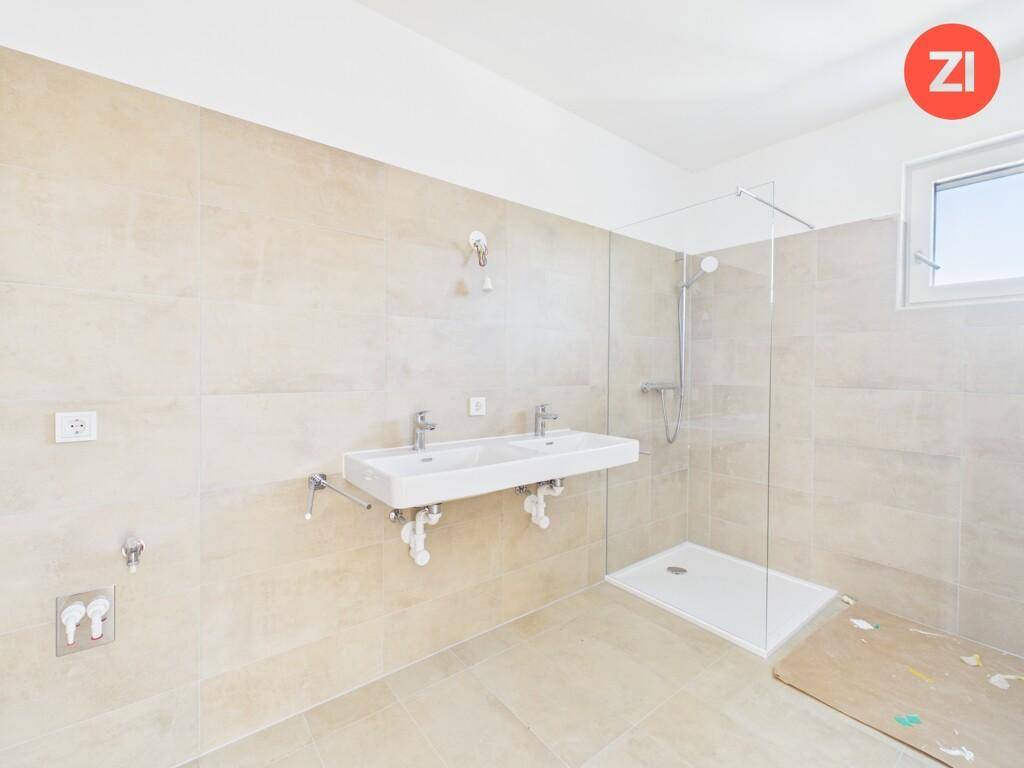 Modernes Badezimmer mit beigen Fliesen, Doppelwaschbecken und einer begehbaren Dusche.