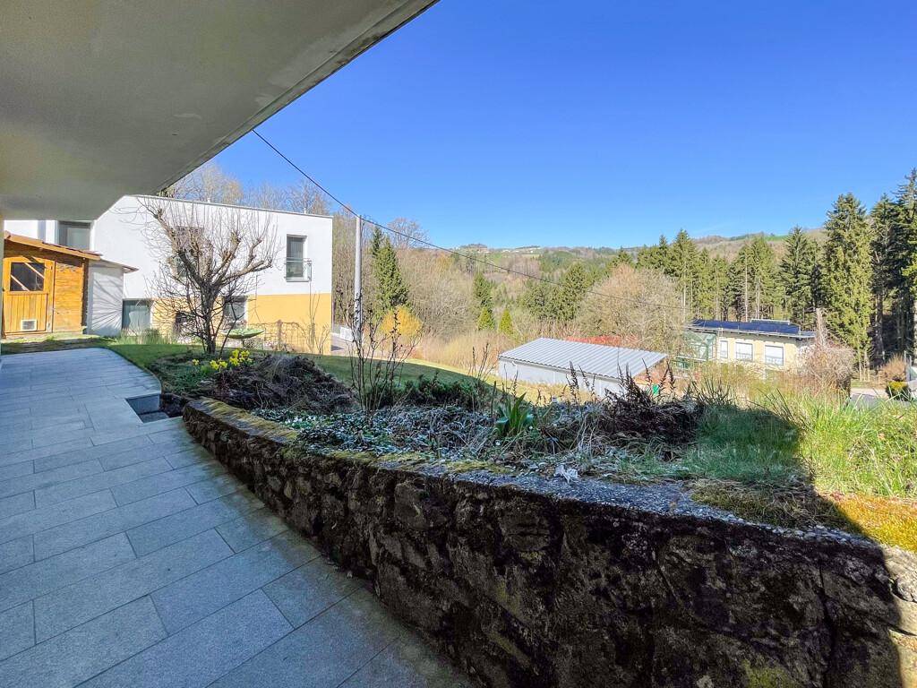 Gepflasterter Außenbereich mit Steinmauer und weitem Blick auf die bewaldete Landschaft.