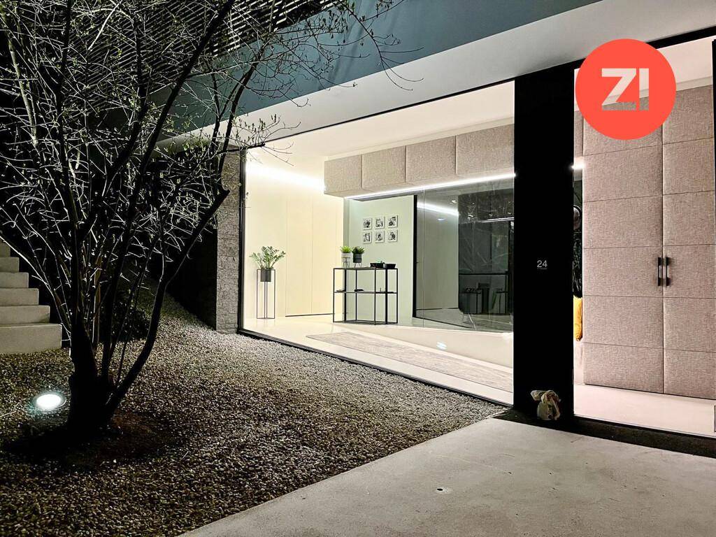 Beleuchteter Eingangsbereich bei Nacht mit minimalistischer Einrichtung und großen Glasflächen.