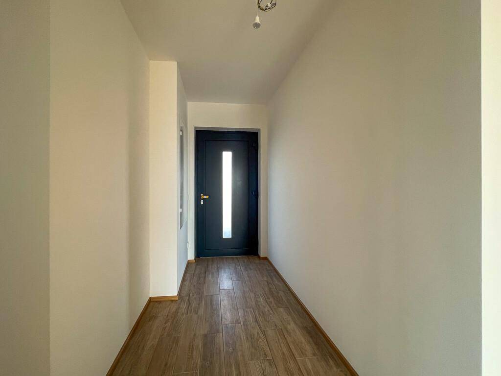 Heller Eingangsbereich mit Holzboden und moderner dunkler Eingangstür mit Glaseinsatz.