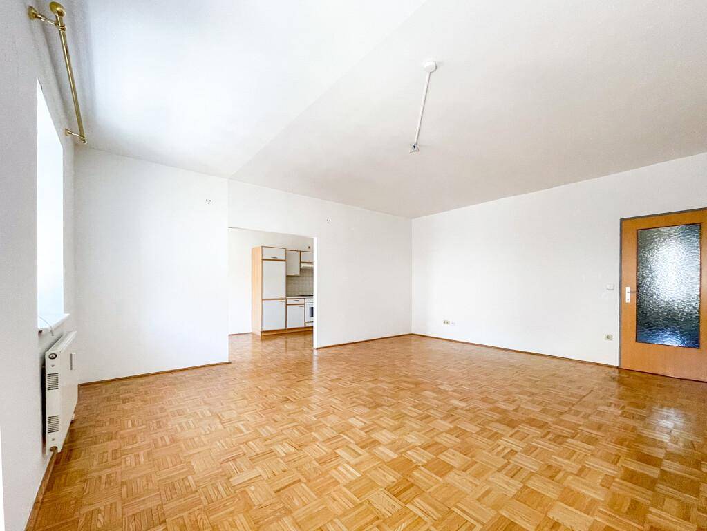 Offener Wohnbereich mit Parkettboden und Blick auf eine angrenzende Küchenzeile.