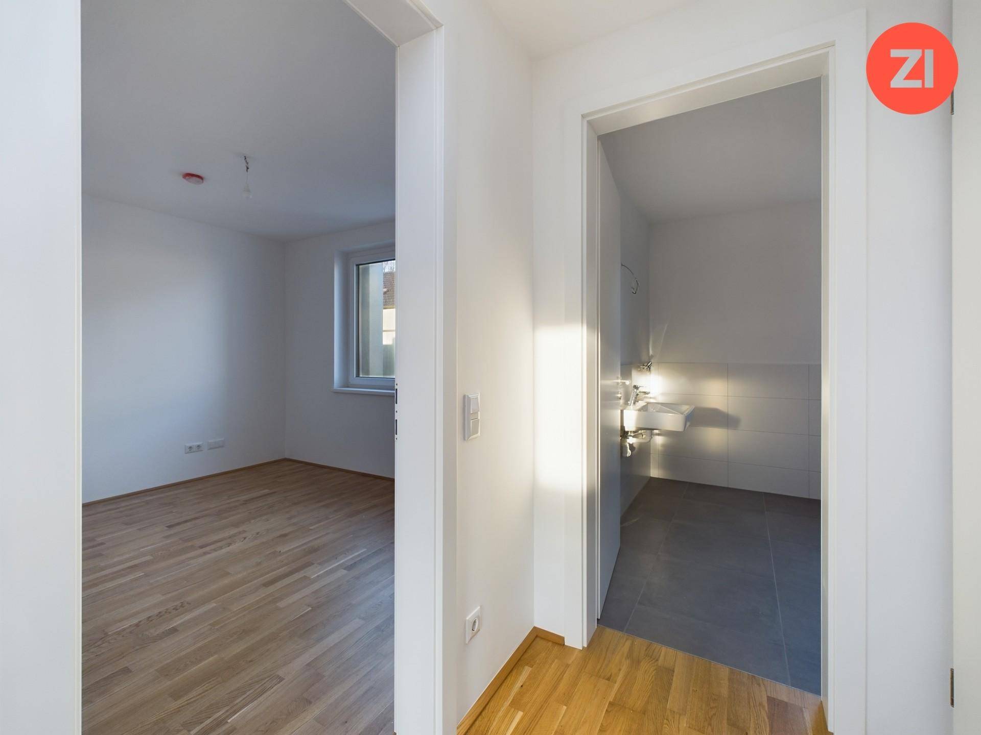 Heller Flur mit Zugang zu einem Zimmer und einem modern gefliesten Badezimmer.