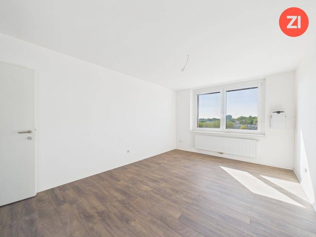 Geräumiges Schlafzimmer mit hellem Laminatboden und Fenster mit Blick ins Grüne.
