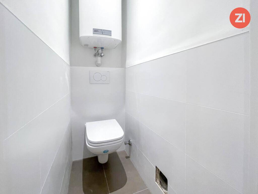 Separates WC mit wandhängender Toilette und weiß gefliesten Wänden, ausgestattet mit Boiler.