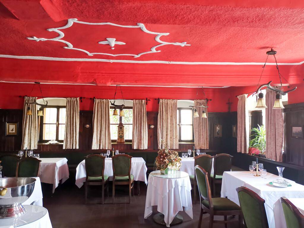 Festlicher Speisesaal mit roter Decke, Stuckelementen und traditionellen Holzvertäfelungen an den Wänden.