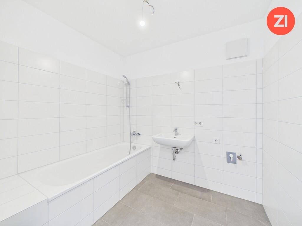 Helles Badezimmer mit weißen Fliesen, Badewanne mit Duschfunktion und Einzelwaschbecken.