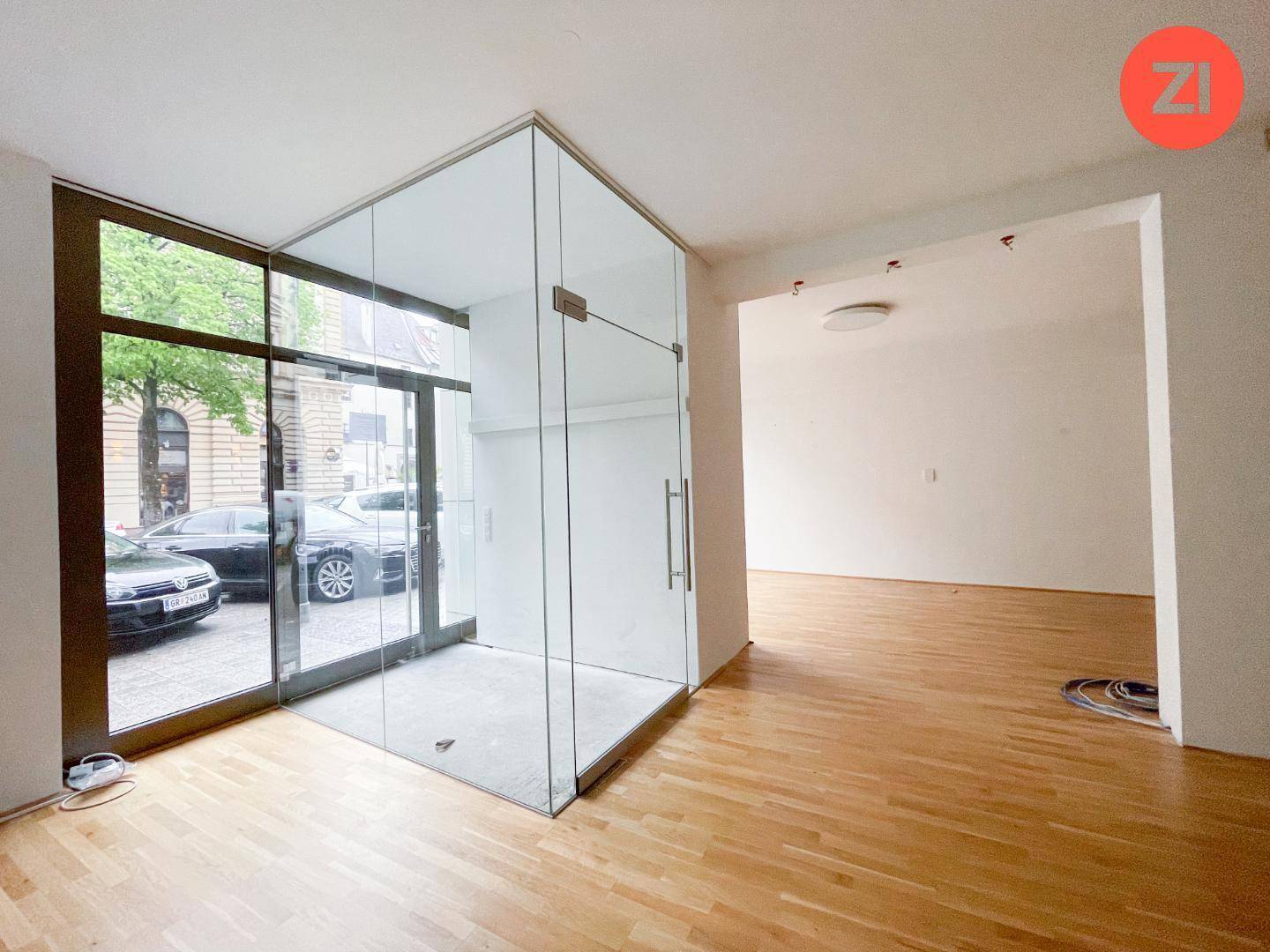 Geräumiger, unmöblierter Gewerberaum mit Holzboden und einer eleganten Glasabtrennung im Eingangsbereich.