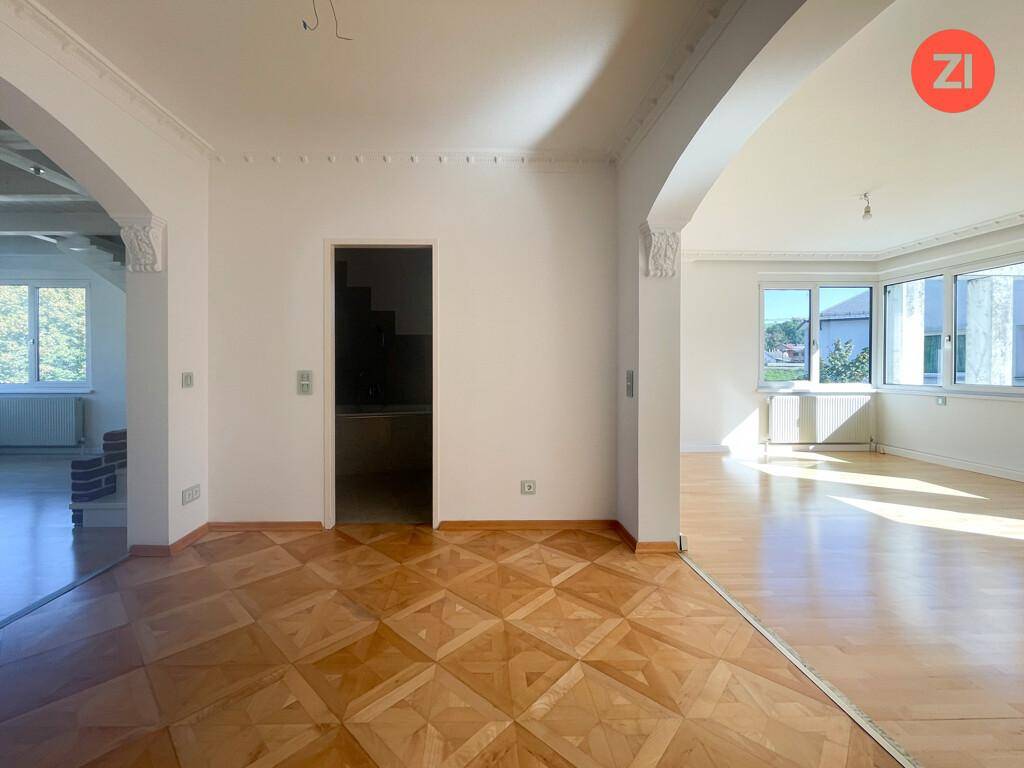 Helle Räume mit unterschiedlichen Parkettböden, verbunden durch einen eleganten Bogen und Stuckdetails an der Decke.