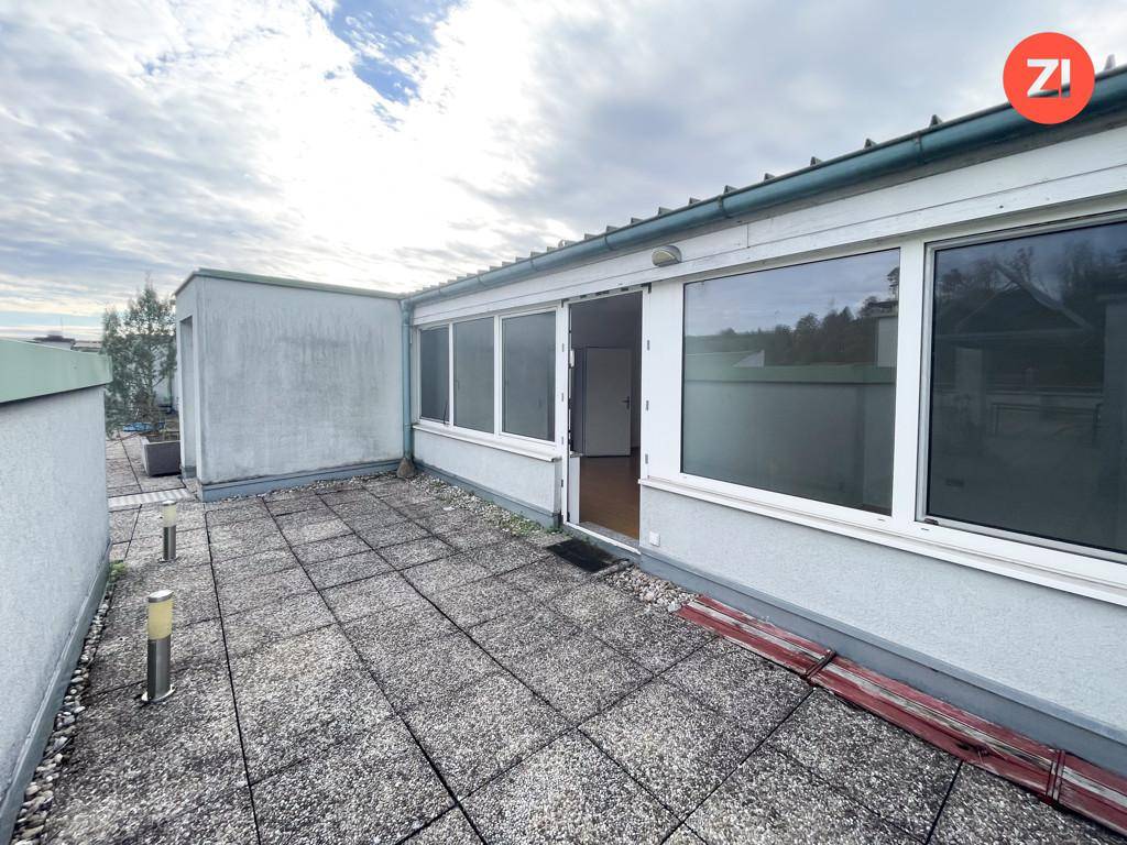 Geräumige Dachterrasse mit Steinplatten und Blick auf die Umgebung unter bewölktem Himmel.