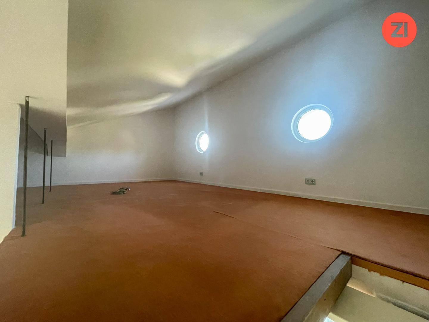Offener Loftbereich mit runden Fenstern und einfacher Bodenfläche, bietet vielseitige Nutzungsmöglichkeiten.