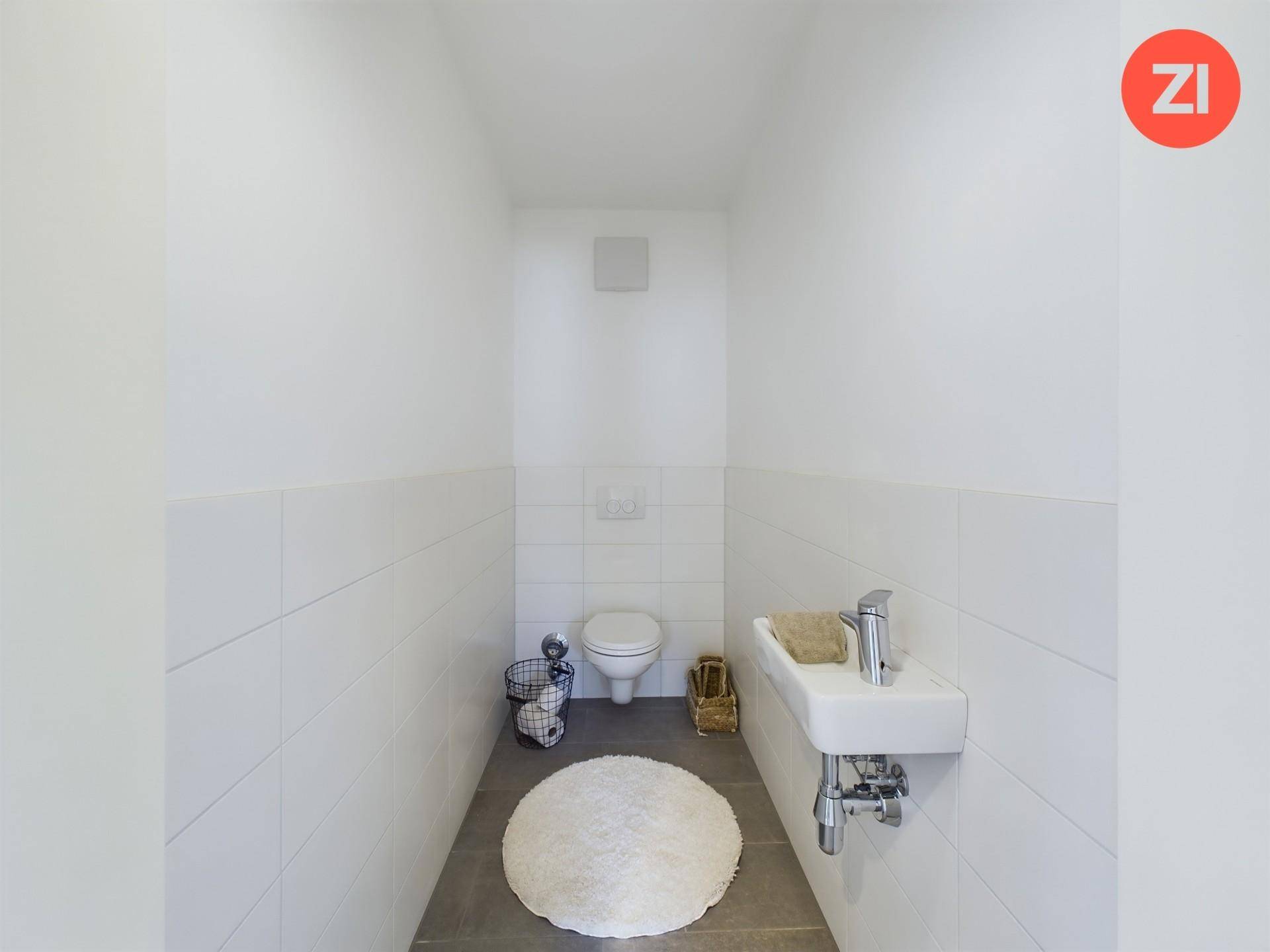 Separates Gäste-WC mit Wand-WC, kleinem Waschbecken und weißen Fliesen.