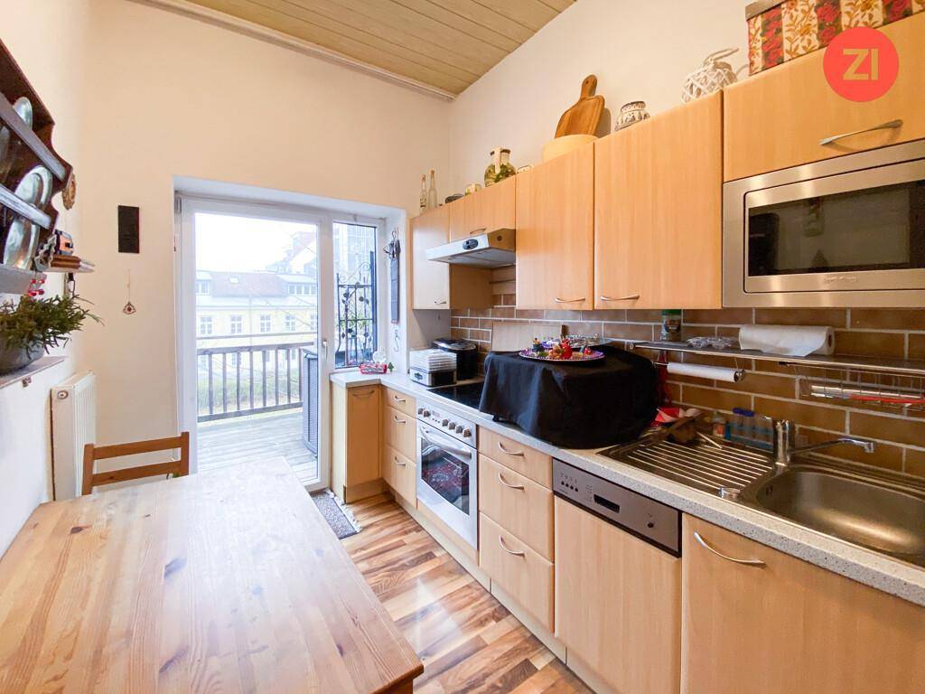 Helle Holzküche mit Essbereich und direktem Zugang zu einem Balkon, ausgestattet mit modernen Geräten.