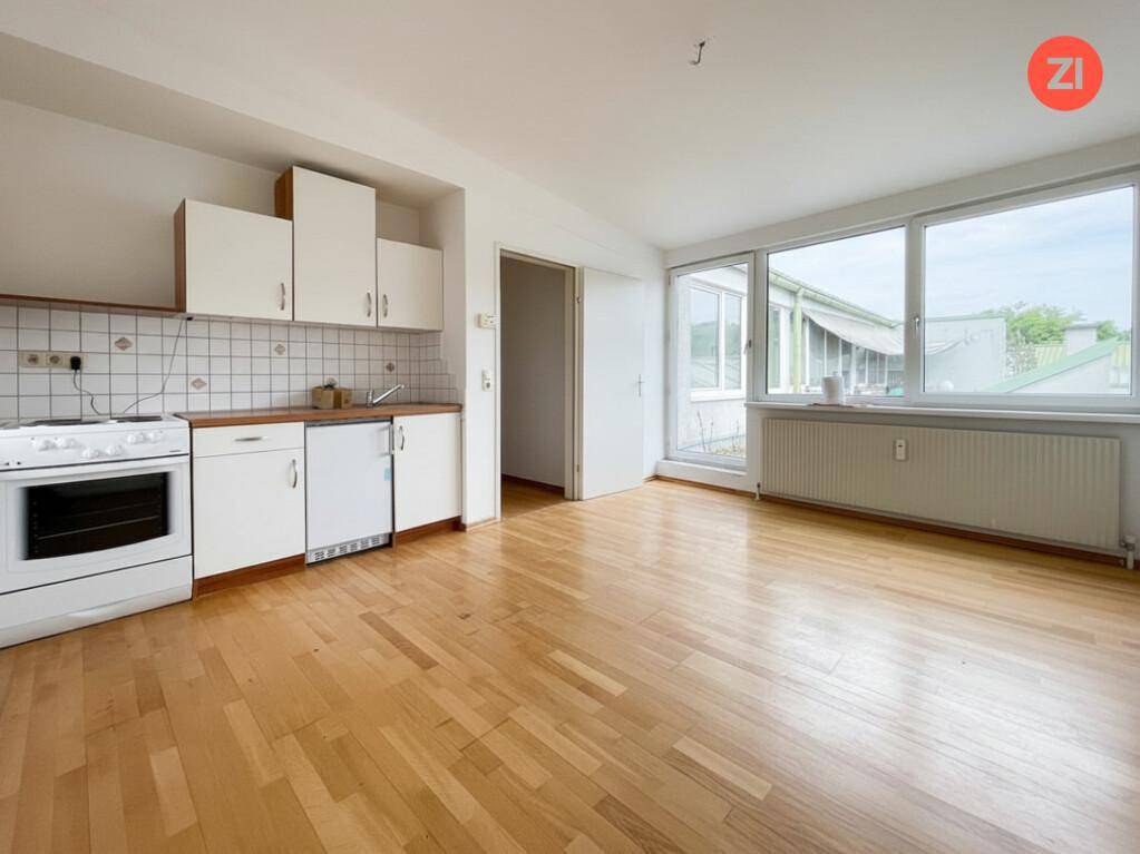 Einfache Küchenzeile in einem hellen Raum mit Holzfußboden und großen Fenstern.
