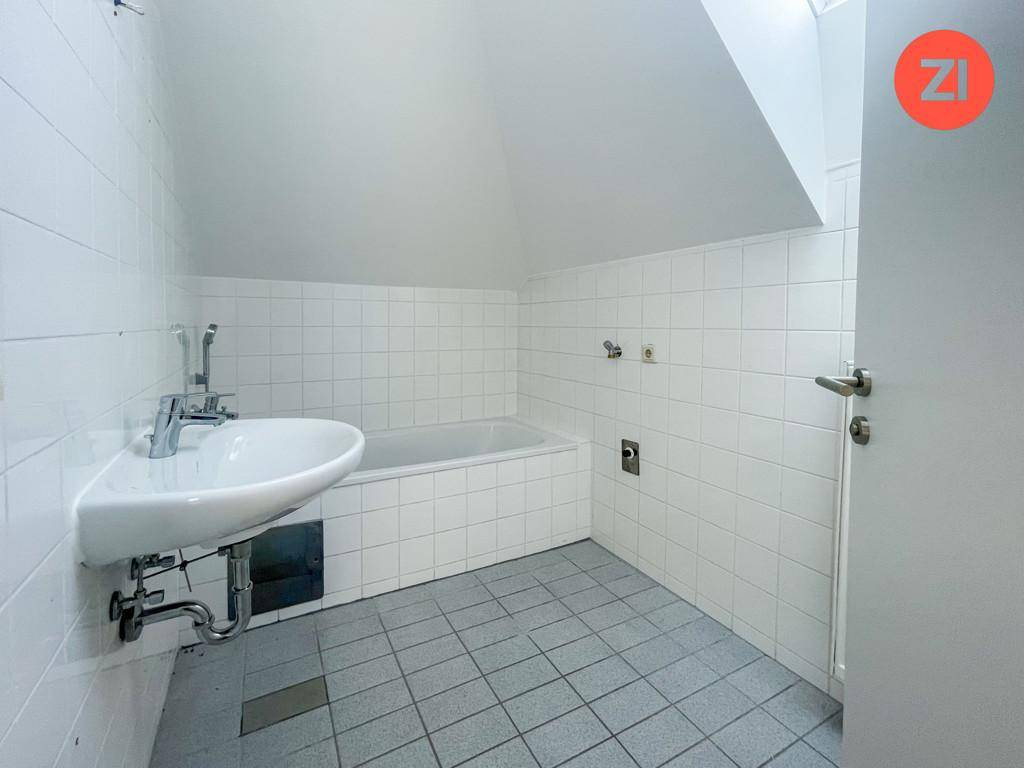Badezimmer mit Badewanne, Waschbecken und weißen Fliesen unter einer Dachschräge.